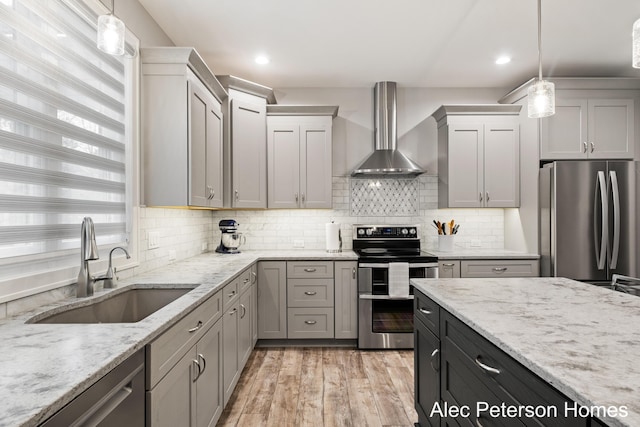 kitchen with appliances with stainless steel finishes, wall chimney range hood, a sink, tasteful backsplash, and decorative light fixtures