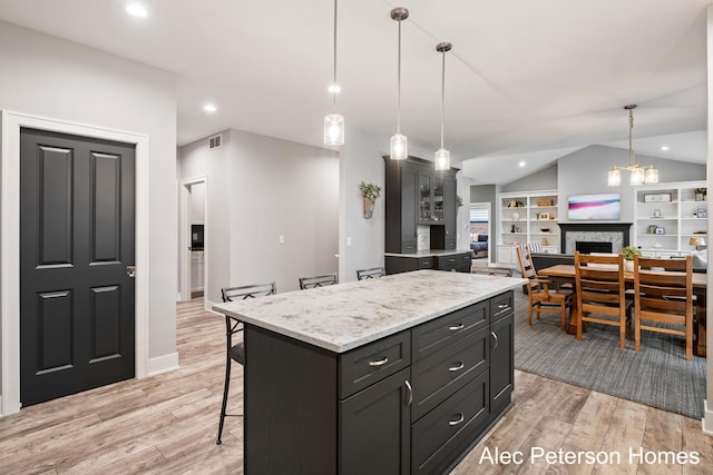 kitchen with vaulted ceiling, light wood-style floors, a breakfast bar, hanging light fixtures, and a fireplace