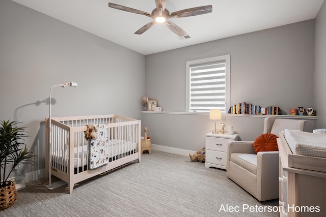 carpeted bedroom with a crib, baseboards, and ceiling fan