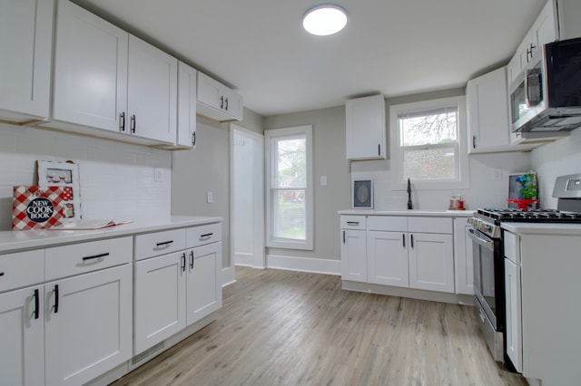 127 Bates St, Jackson, MI 49202 - kitchen with stainless steel appliances, light countertops, light wood-type flooring, backsplash, and white cabinets