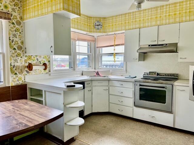 kitchen featuring wallpapered walls, under cabinet range hood, stainless steel electric range oven, a sink, and light countertops