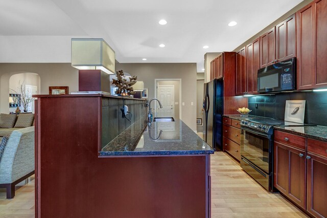 kitchen featuring black appliances, dark brown cabinets, a sink, light wood-style floors, and dark stone counters