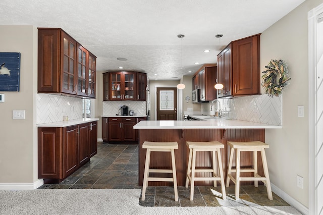 kitchen featuring baseboards, tasteful backsplash, a peninsula, glass insert cabinets, and a sink