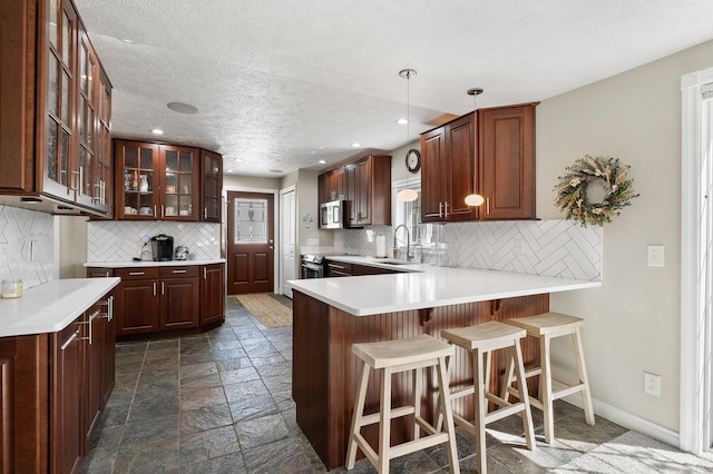 kitchen with a sink, stainless steel microwave, a peninsula, stone tile flooring, and decorative backsplash