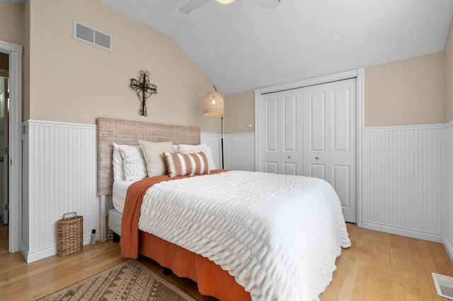 bedroom with lofted ceiling, light wood-style flooring, a closet, wainscoting, and a ceiling fan