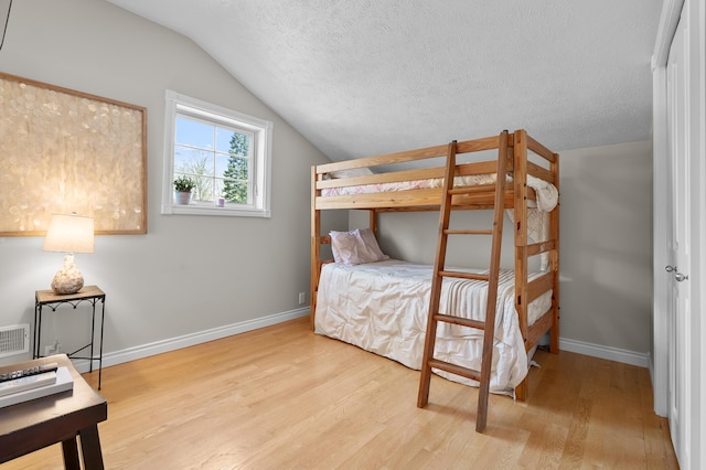 bedroom featuring wood finished floors, lofted ceiling, baseboards, and a textured ceiling