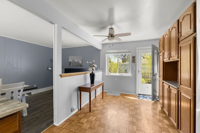 entryway featuring baseboards, a ceiling fan, and wooden walls