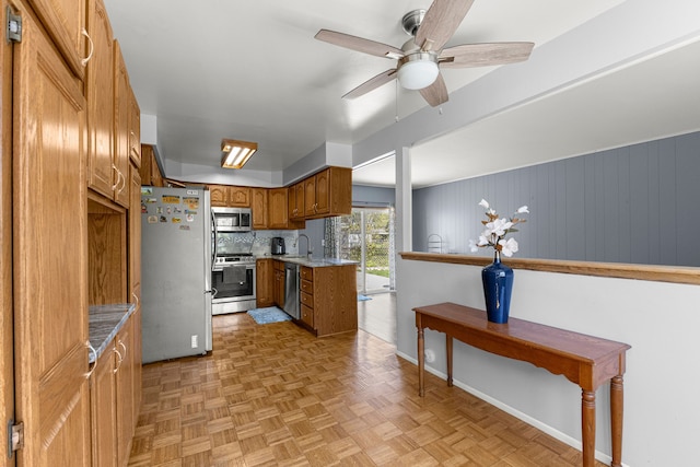 kitchen with appliances with stainless steel finishes, brown cabinets, ceiling fan, baseboards, and a sink