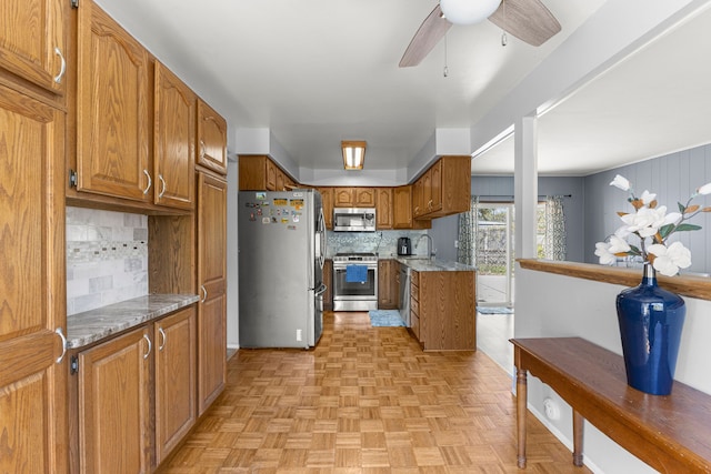 kitchen featuring stainless steel appliances, brown cabinets, tasteful backsplash, a sink, and a ceiling fan