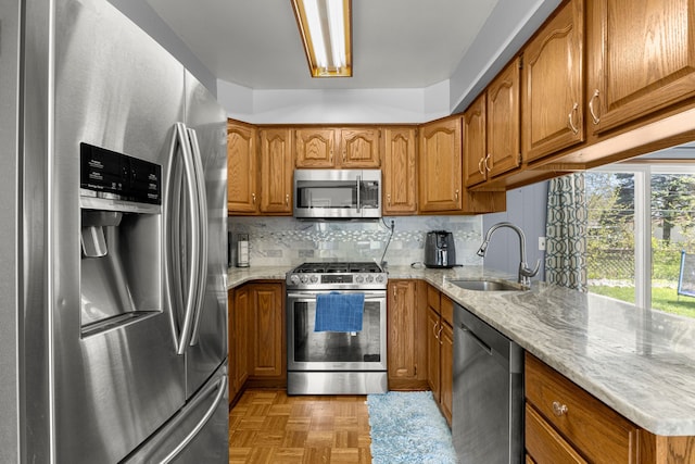 kitchen with stainless steel appliances, a sink, brown cabinetry, light stone counters, and backsplash