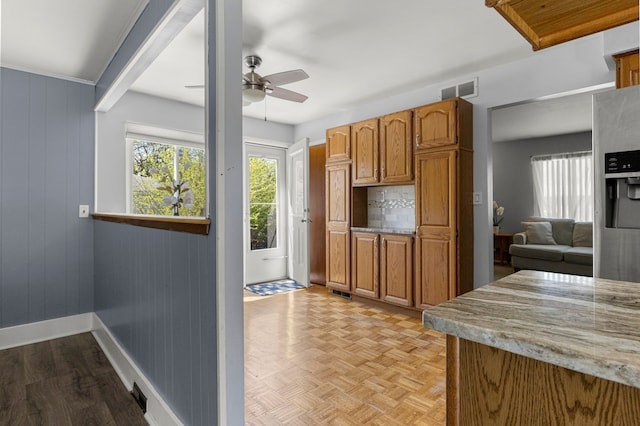 kitchen with baseboards, a ceiling fan, brown cabinetry, and light stone countertops