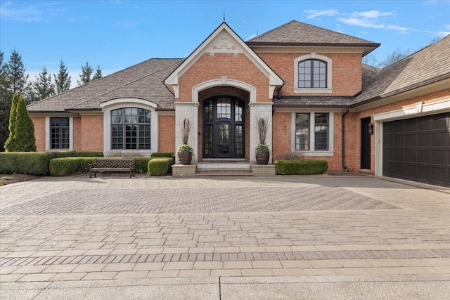french country home featuring brick siding, decorative driveway, and a garage