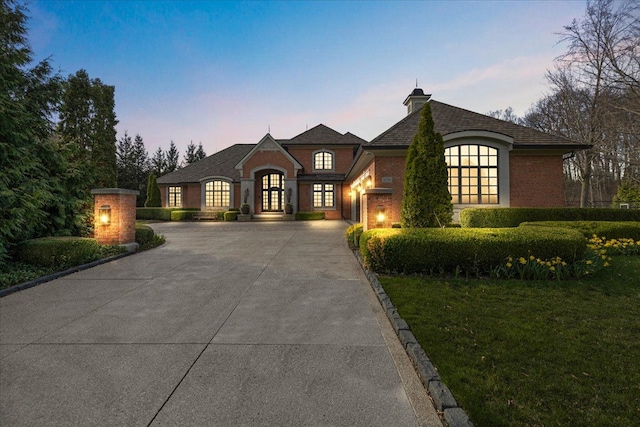 french country home with driveway, brick siding, french doors, and a lawn