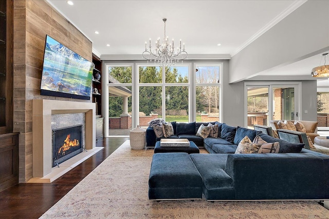 living room featuring a chandelier, crown molding, plenty of natural light, dark wood-style flooring, and a warm lit fireplace