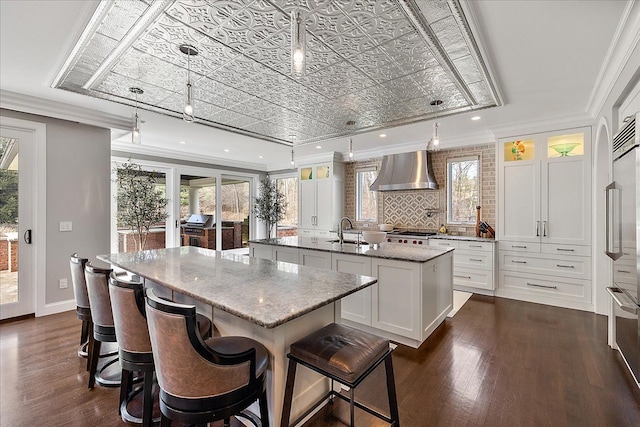 kitchen featuring an island with sink, a sink, dark wood-style floors, wall chimney exhaust hood, and white cabinets