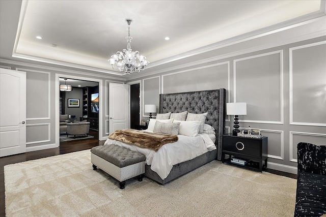 bedroom with a decorative wall, a tray ceiling, a chandelier, recessed lighting, and crown molding
