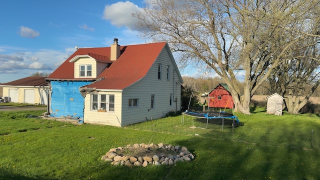 rear view of property featuring a trampoline, a yard, and a chimney