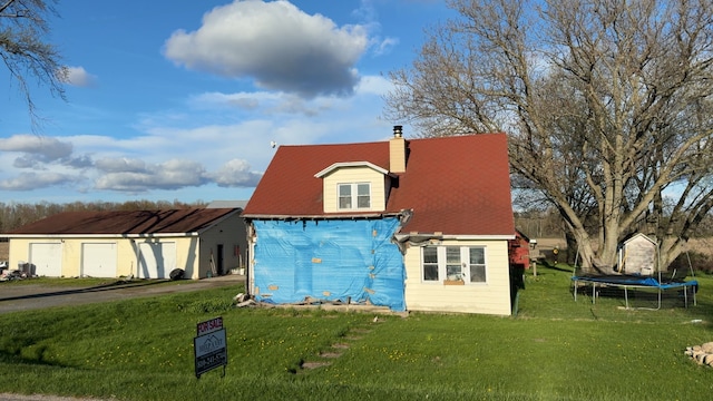 rear view of property with a trampoline, a yard, a garage, a chimney, and driveway