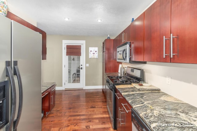 kitchen with stainless steel appliances, dark wood finished floors, baseboards, reddish brown cabinets, and dark stone counters