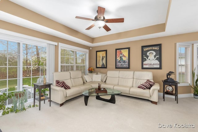 living room with carpet, ceiling fan, a tray ceiling, and baseboards