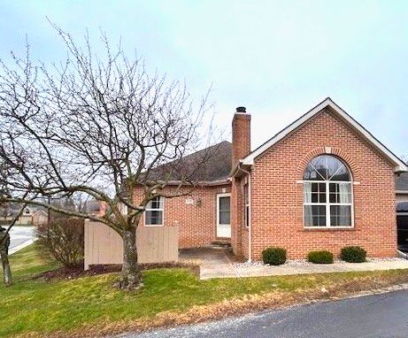 view of side of property featuring brick siding, a chimney, a patio, and a lawn