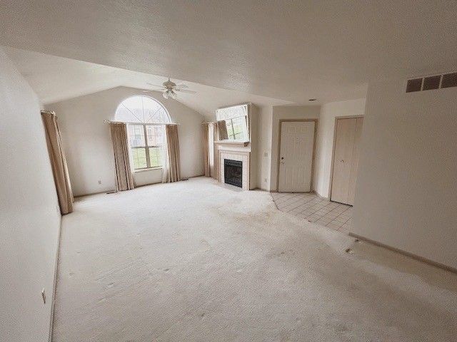 unfurnished living room featuring ceiling fan, carpet floors, a fireplace, and lofted ceiling
