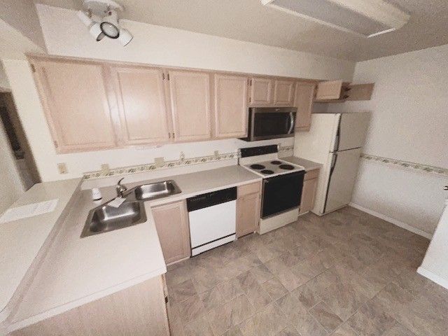 kitchen with white appliances, light brown cabinetry, light countertops, and a sink