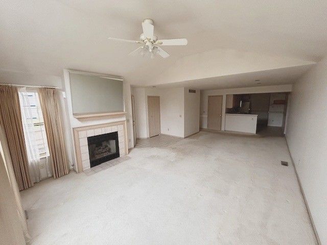unfurnished living room with a tile fireplace, a ceiling fan, and lofted ceiling