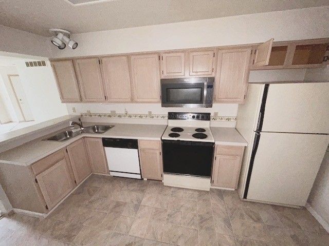 kitchen featuring white appliances, light countertops, a sink, and light brown cabinets
