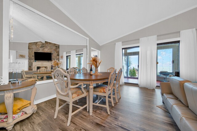 dining space with wood finished floors, lofted ceiling, plenty of natural light, a fireplace, and crown molding