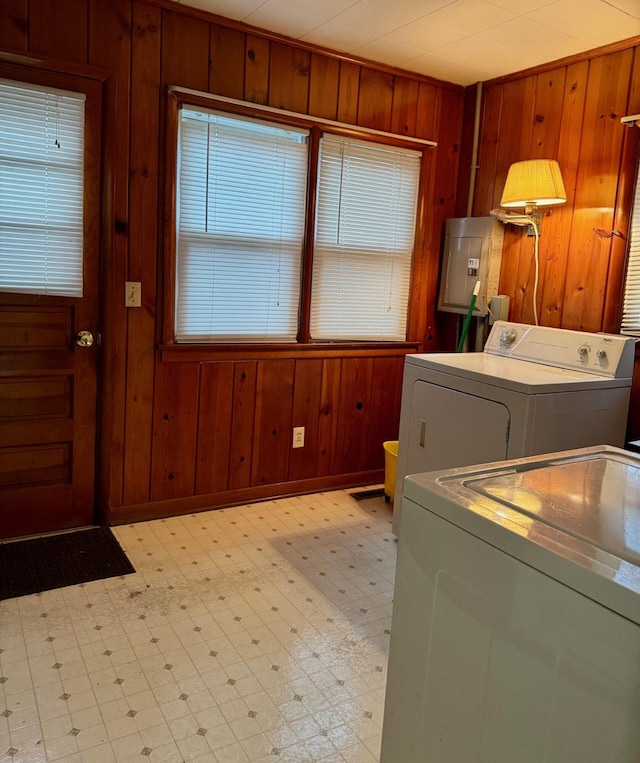 laundry area featuring wood walls, light flooring, electric panel, washing machine and clothes dryer, and baseboards