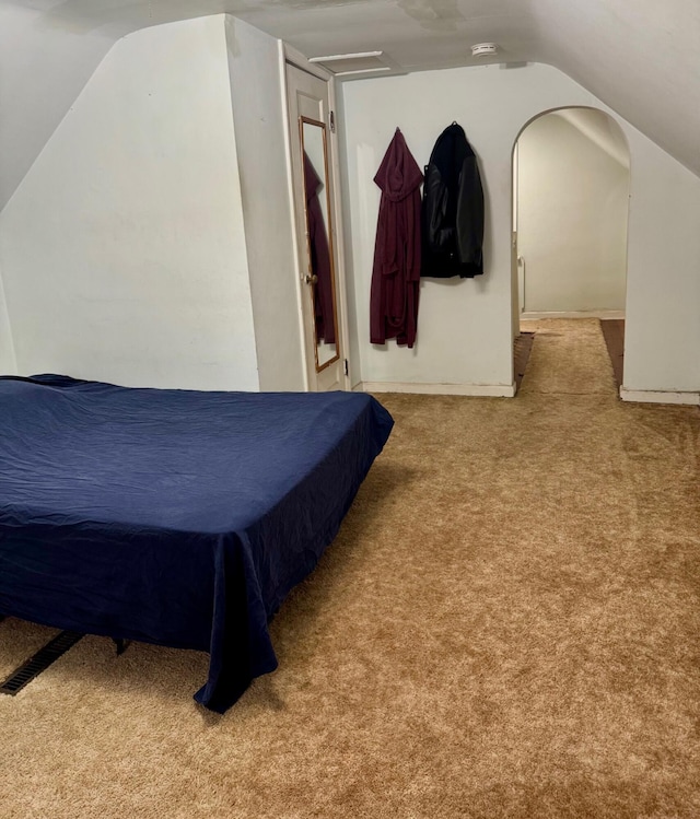 bedroom with carpet flooring, lofted ceiling, arched walkways, and baseboards