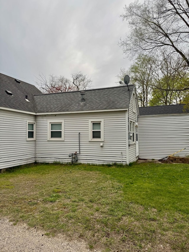 back of house with roof with shingles and a lawn