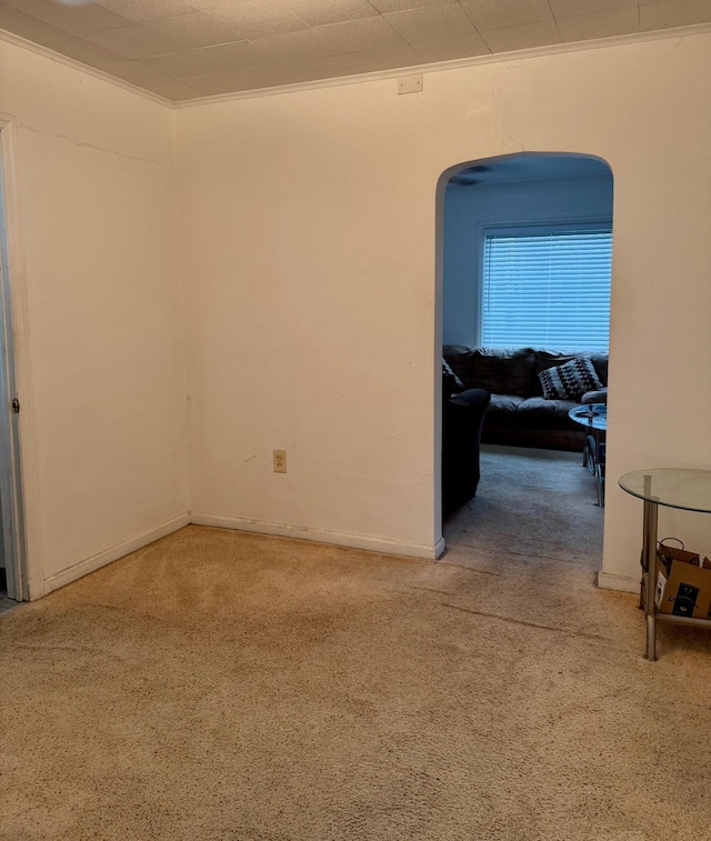 empty room with carpet flooring, arched walkways, crown molding, and baseboards