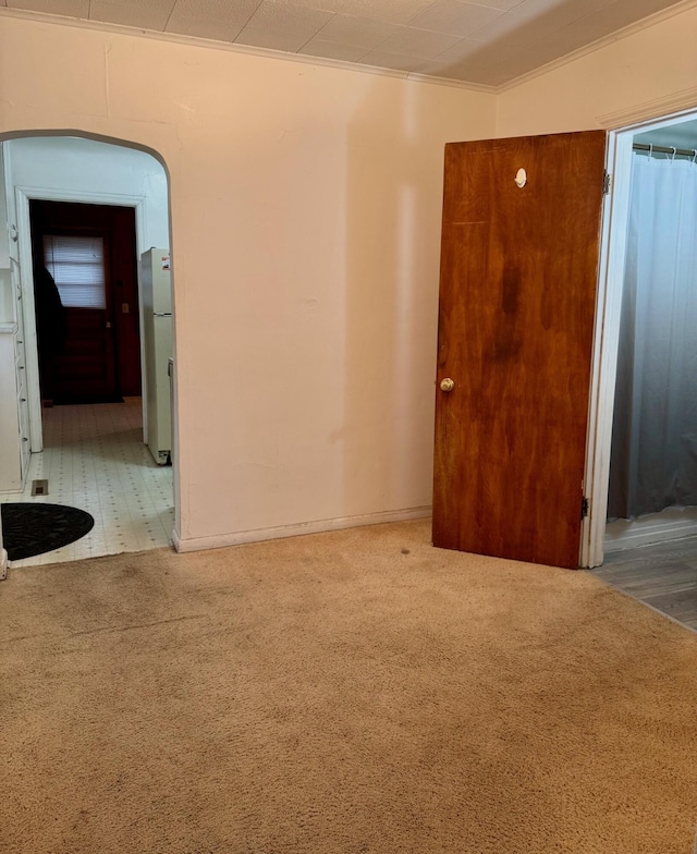 carpeted spare room featuring crown molding and arched walkways