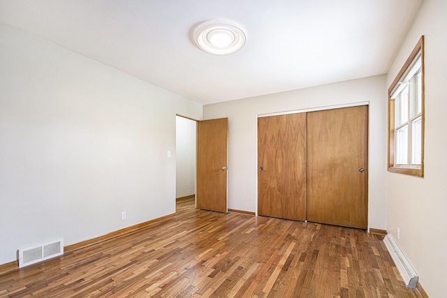 2228 Washington Ave, Saint Joseph, MI 49085 - unfurnished bedroom with a baseboard radiator, wood finished floors, a closet, and baseboards