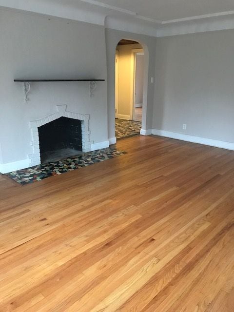 17311 Santa Rosa Dr, Detroit, MI 48221 - unfurnished living room featuring a brick fireplace, wood finished floors, arched walkways, and baseboards