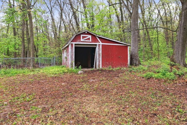 view of outbuilding featuring fence, an outdoor structure, and a wooded view