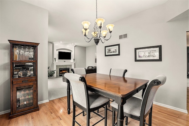 1079 Trailside Blvd, Wixom, MI 48393 - dining room featuring light wood-style floors, a chandelier, baseboards, and a lit fireplace