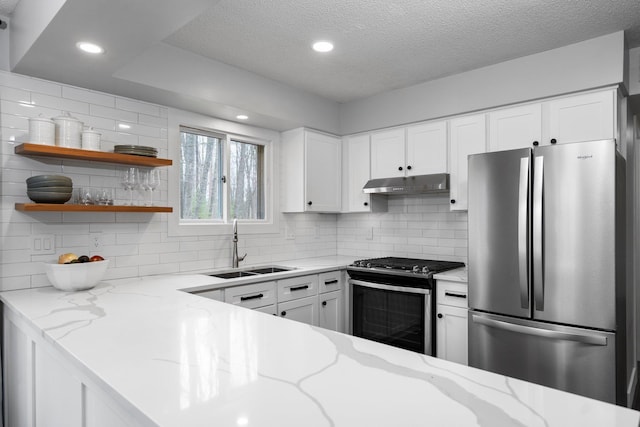 kitchen with stainless steel appliances, a sink, under cabinet range hood, decorative backsplash, and a textured ceiling