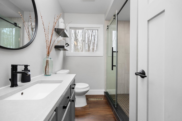bathroom featuring a shower stall, toilet, wood finished floors, vanity, and baseboards
