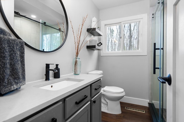 bathroom with toilet, vanity, a shower stall, wood finished floors, and baseboards