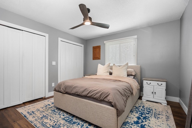 bedroom featuring two closets, wood finished floors, baseboards, and a ceiling fan