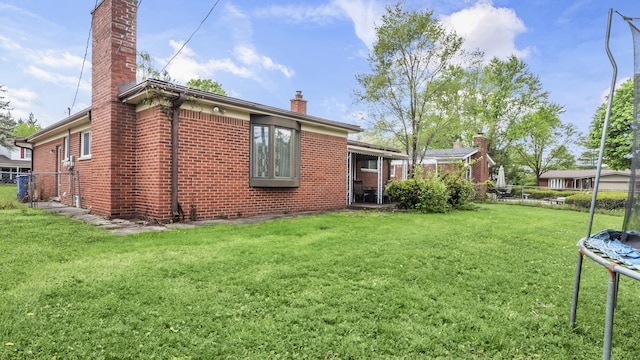 rear view of house featuring a trampoline, a chimney, and brick siding