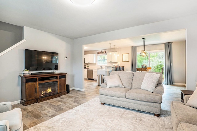 living area featuring light wood-style floors, baseboards, and a glass covered fireplace