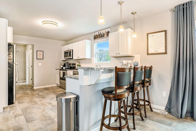 kitchen featuring appliances with stainless steel finishes, a peninsula, a kitchen breakfast bar, white cabinetry, and light wood-style floors