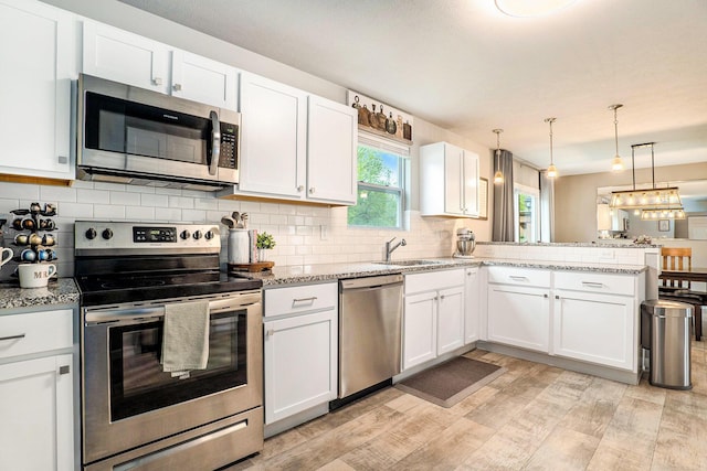 kitchen featuring appliances with stainless steel finishes, a peninsula, light wood-style flooring, and white cabinetry
