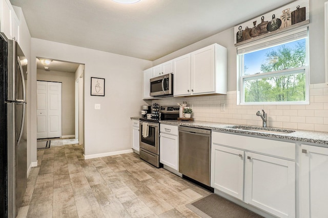 kitchen with appliances with stainless steel finishes, a sink, decorative backsplash, white cabinetry, and light wood-style flooring