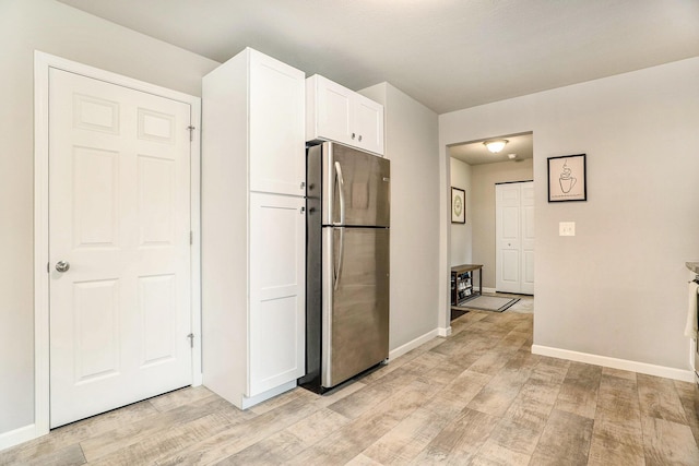 kitchen featuring freestanding refrigerator, light wood-style flooring, white cabinets, and baseboards