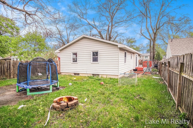 view of side of property with a trampoline, an outdoor fire pit, and a wooden deck